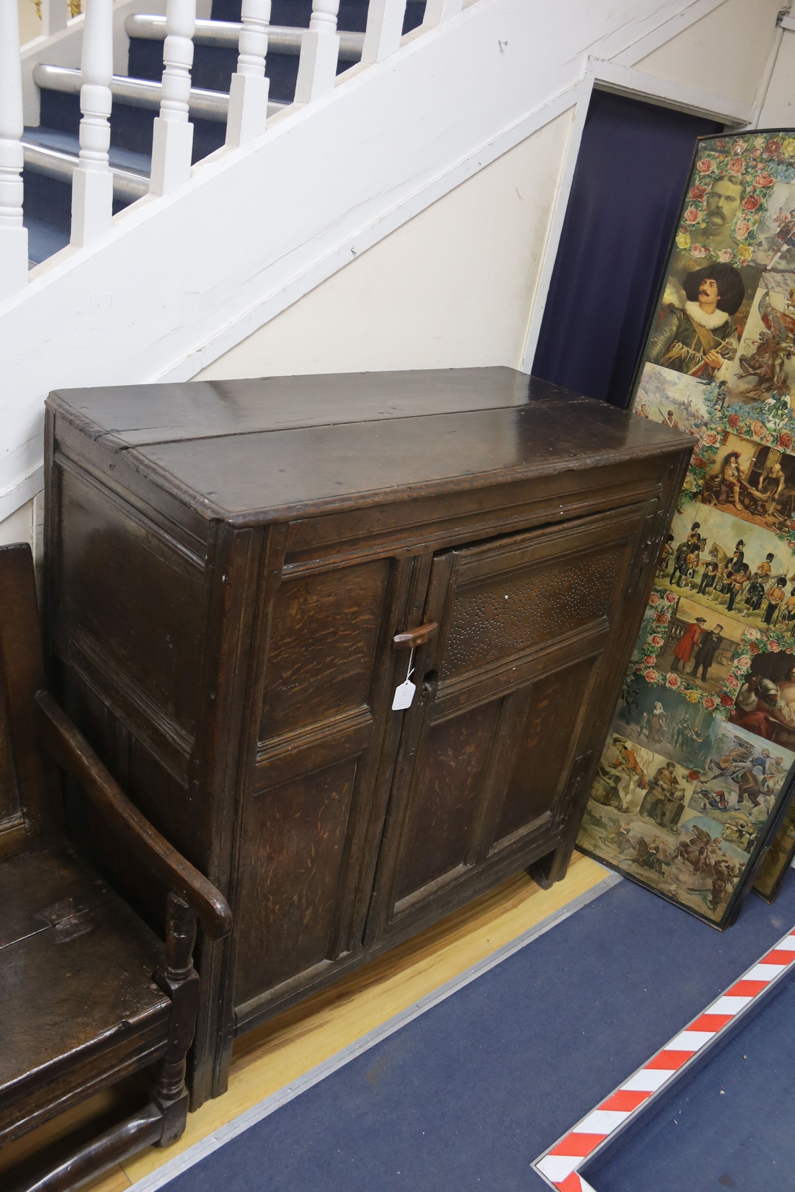 An early joined oak food cupboard, the planked top above a single hinged pierced panelled door, width 112cm, depth 55cm, height 115cm